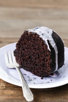 a piece of chocolate cake with white frosting on a plate next to a fork