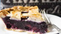 a slice of blueberry pie on a white plate with a fork and wine bottle in the background