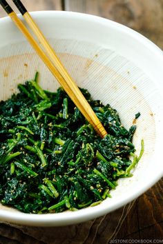 a white bowl filled with greens and chopsticks