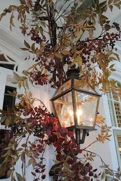 a lamp hanging from the side of a building with leaves and branches on it's sides