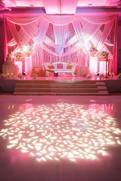 an indoor wedding venue with pink lighting and white drapes