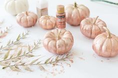 some pink pumpkins sitting on top of a white table next to leaves and glue