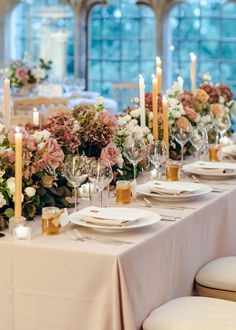 a table set with flowers and candles for a formal dinner or wedding reception in front of a large window