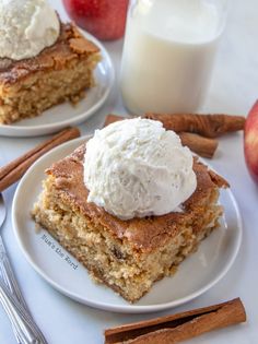 two pieces of cake on plates next to an apple, cinnamon and glass of milk