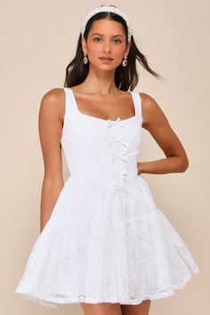 An awe-inspiring look like the Rare London Truly Flawless White Lace Sleeveless Bow Bustier Mini Dress deserves to be shown off and admired! This seriously romantic lace dress starts with wide straps, a square neckline, and a bustier-style bodice with supportive boning throughout and a row of dainty bows that run along the center. The fitted waist tops a tiered, skater-style skirt (with a hidden layer of organza for volume) that ends at a flirty mini hem. Hidden back zipper/clasp. Fit: This garm Lace Corset Dress With Lace-up Back And Sweetheart Neckline, Lace Corset Dress With Lace Patchwork, Mini Length, Lace Corset Dress With Lace Patchwork, Mini Lace Corset Dress With Lace Patchwork, Square Neck Lace Dress With Lace Patchwork, Chic Lace Dress With Square Neck, Flirty Lace Mini Dress With Lace Bodice, Mini Length Lace Corset Dress With Lace Trim, Fitted Lace Dress With Corset Back For Summer