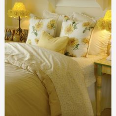 a bed with yellow and white pillows on top of it next to a night stand