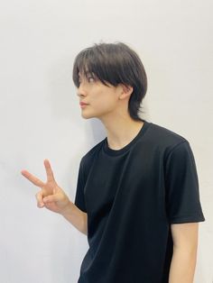 a young man standing in front of a white wall making the peace sign with his fingers