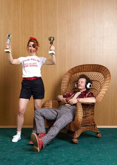 a man sitting in a chair next to a woman holding up two trophies while she is on her lap