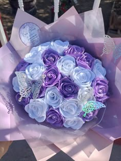 a bouquet of purple and white roses with butterflies on it in someone's hand