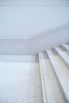 a cat sitting on top of a white set of stairs next to a cement wall