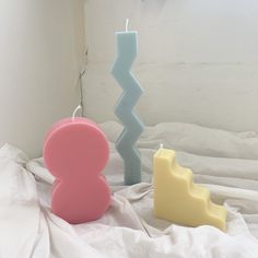 two candles sitting on top of a bed next to each other in front of a white wall