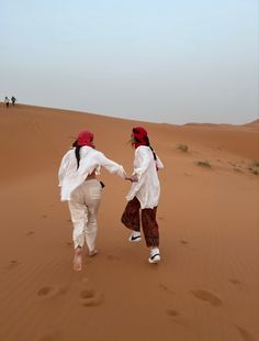 two people in white clothing are walking through the desert