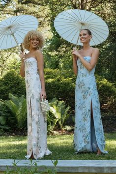 two women standing in the grass with umbrellas over their heads and one holding a purse