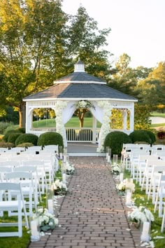 an outdoor wedding venue with white chairs and flowers on the aisle, surrounded by greenery