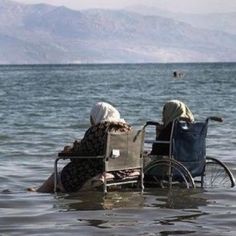 two people sitting in a wheel chair in the water