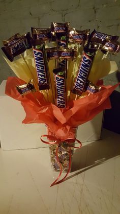 a vase filled with candy bars and wrapped in orange paper on top of a table