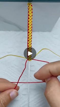 two hands are working on a piece of paper that has been stitched together with red thread