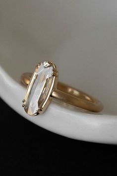 a gold ring with an oval cut diamond on the front and side, sitting on a white plate