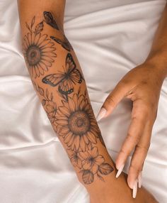 a woman's arm with sunflowers and butterflies tattooed on it, sitting on a bed