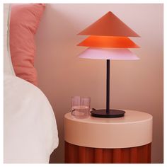 a table with a lamp on it next to a glass cup and pink throw pillow