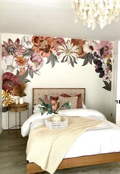 a bed sitting under a chandelier next to a wall with flowers on it