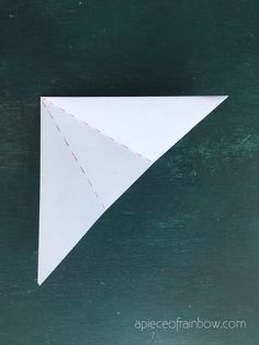 an origami paper triangle on a green surface with red stitching around the edges