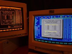 two old computer monitors sitting next to each other on a desk in a dark room