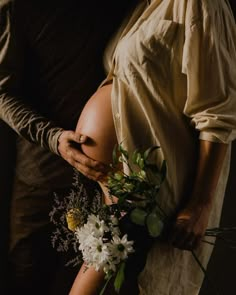 a pregnant woman holding a bouquet of flowers next to a man in a brown shirt