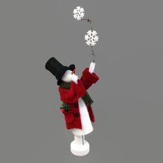 a snowman with a red jacket and black hat holding a white flower in his hand