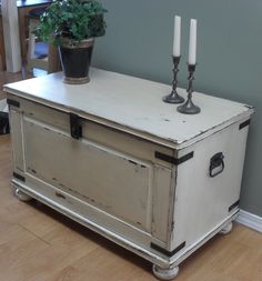 an old trunk with two candles on top and a potted plant next to it