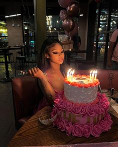 a woman sitting in front of a birthday cake with candles on it and pink roses