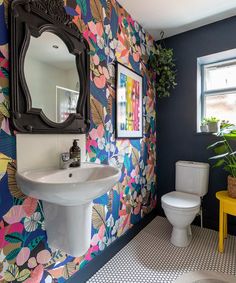 a colorful bathroom with floral wallpaper and white toilet, sink and mirror on the wall