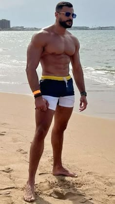 a man standing on top of a sandy beach next to the ocean wearing swim trunks