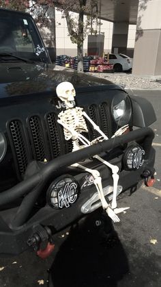 a skeleton sitting on the hood of a black jeep parked in front of a building