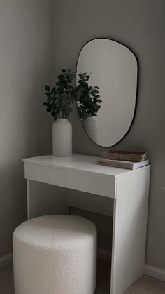 a white vanity table with a round mirror above it and a plant in a vase on top