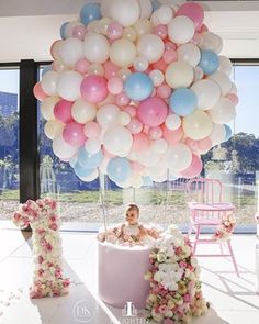 a baby in a tub surrounded by balloons and flowers on a table with the letter h