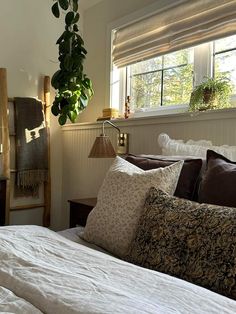 a bed with white sheets and pillows in front of a window filled with potted plants