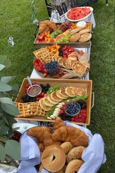 an assortment of pastries and fruit on display in baskets at a picnic table outdoors