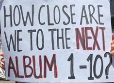 a person holding a sign that says how close are we to the next album 1 - 10?