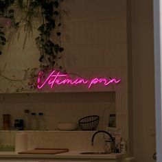 a pink neon sign above a sink in a kitchen next to a plant on the wall