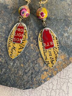 a pair of earrings with words and flowers hanging from it's sides on a rock