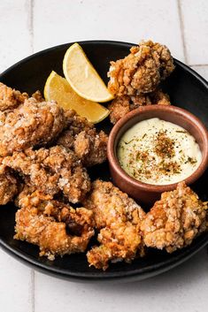 fried chicken and dipping sauce on a black plate with lemon wedges next to it