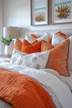 a bed with orange and white pillows on top of it next to two framed pictures