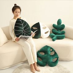 a woman sitting on a couch reading a book next to two green mask shaped pillows