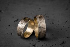 two gold wedding rings sitting on top of a black surface with holes in the middle