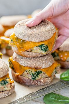 a hand picking up a cheeseburger from a stack of mini sandwiches on a cooling rack