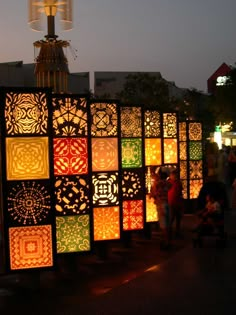 many different colored lights are lit up on the street at night with people walking by