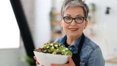 a woman wearing glasses holding a bowl of salad