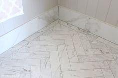 a bathroom with white marble flooring and herringbone tile on the walls, along with a window