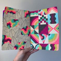 a hand holding an open book with colorful designs on it